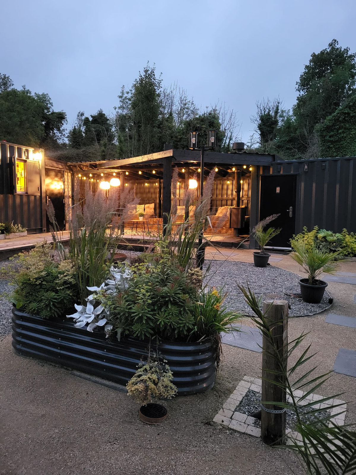 The covered lounge lit up at dusk, with a raised planter in front