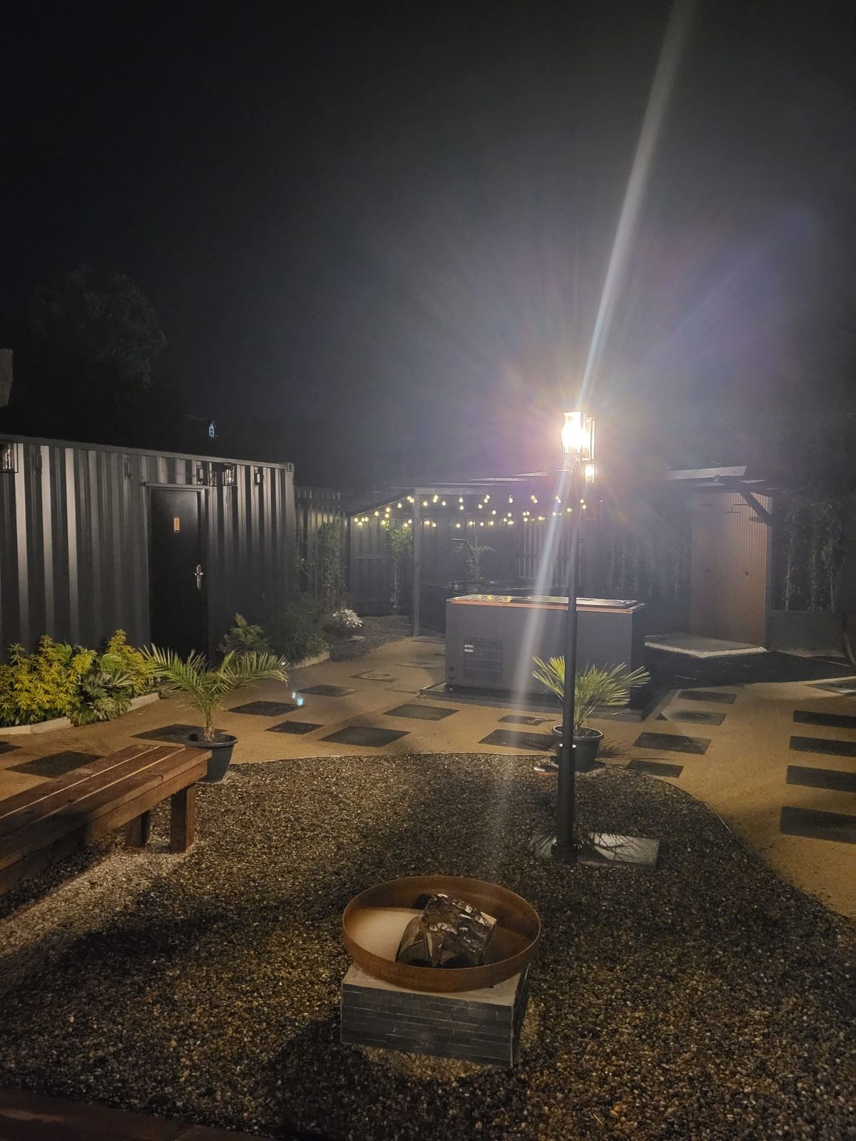 The courtyard at night, lit by a lamp, with the fire bowl in the foreground