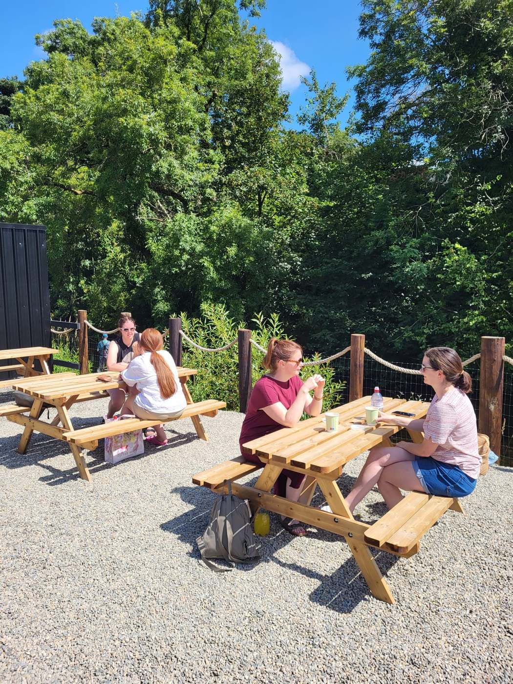 Friends chatting over coffee at picnic tables by the river