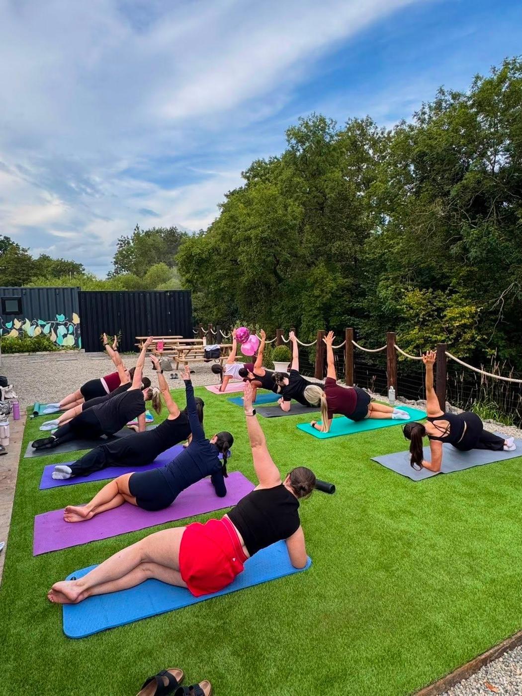 An outdoor pilates class holding side planks on the lawn