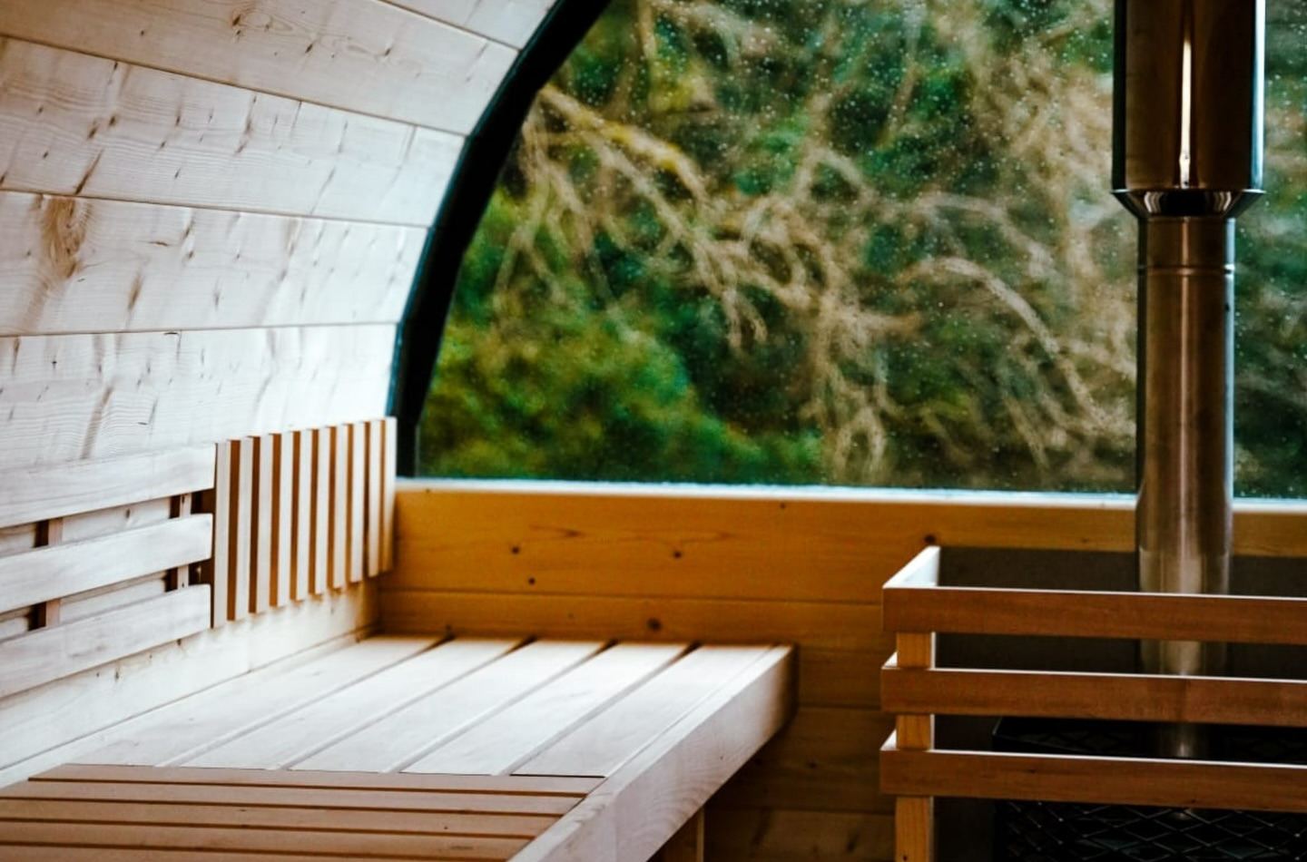 Inside the barrel sauna: timber benches, the stove and a window onto the trees
